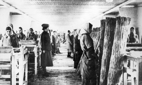 Unter Aufsicht einer Kapo binden so genannte "Zigeunerinnen" in Zwangsarbeit im KZ Ravensbrück Binsenmatten